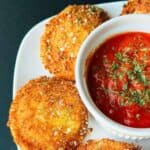 Fried ravioli on a white plate with a small bowl of sauce