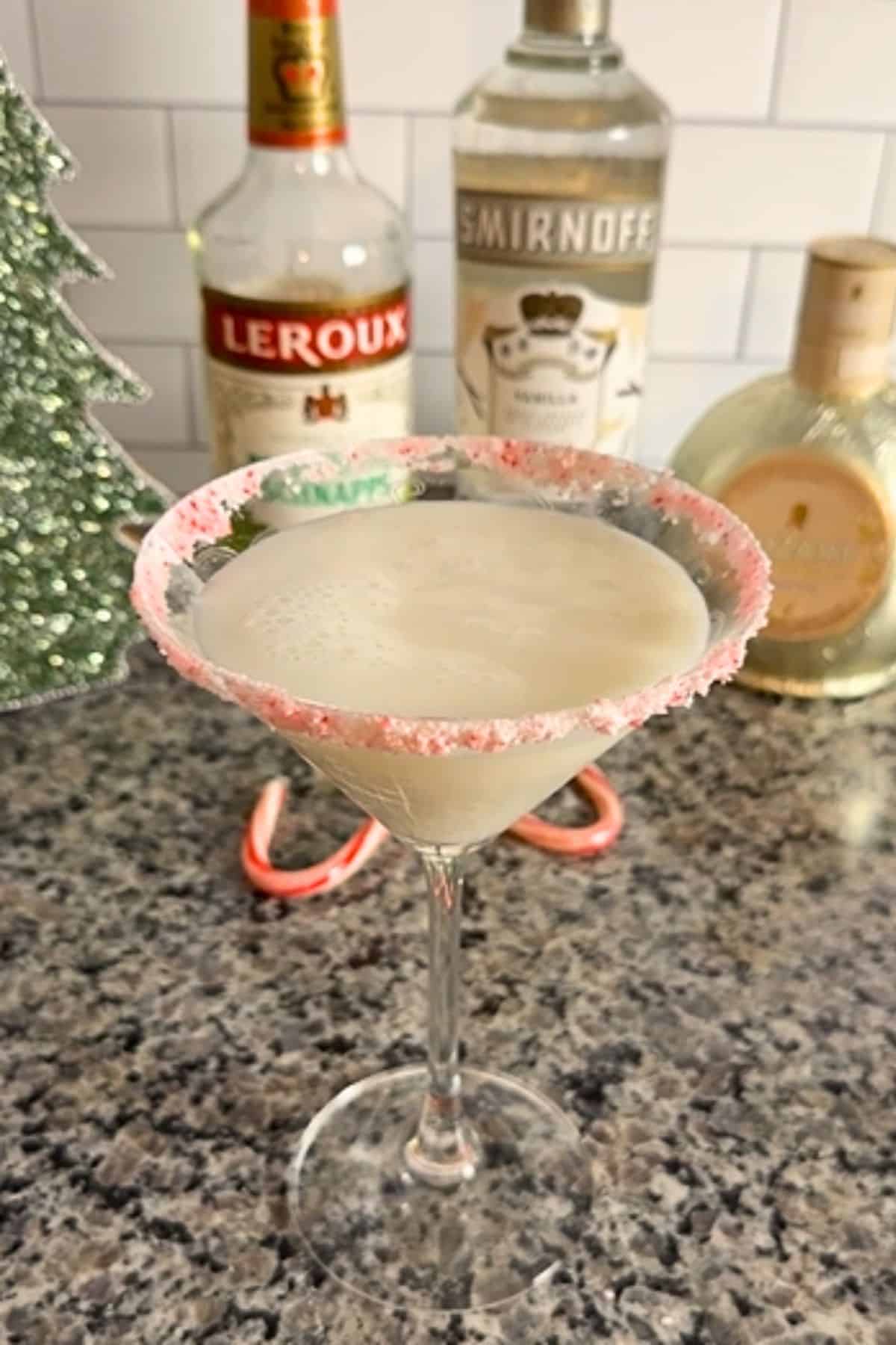 White chocolate candy cane martini in a glass with the ingredients in bottles in the background