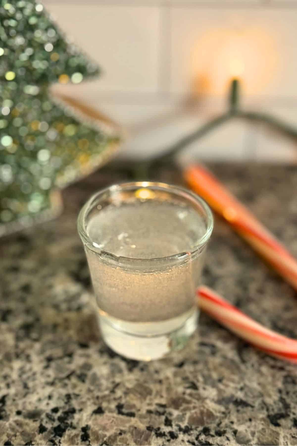 A polar bear shot in a shot glass with a candy cane in the background