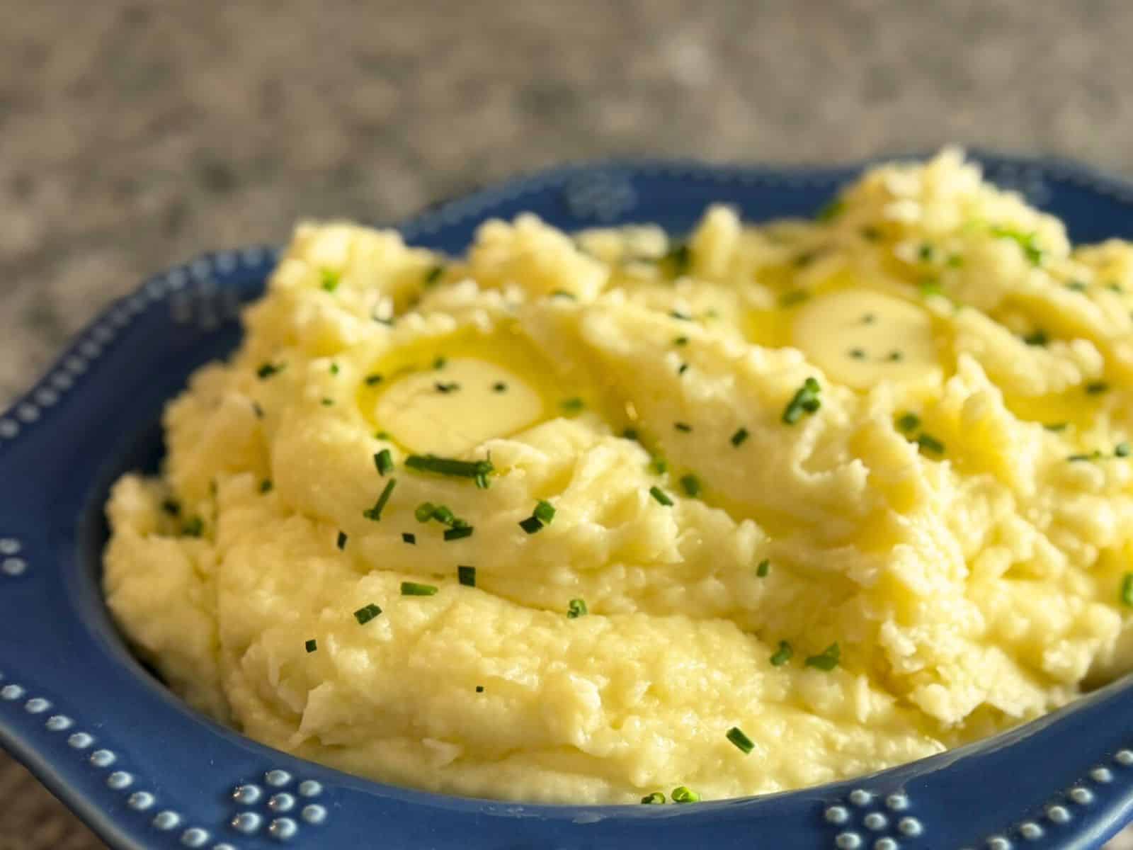 A blue bowl full of creamy garlic mashed potatoes garnished with chives