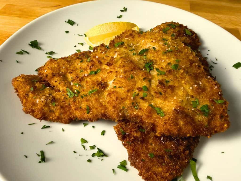 Italian breaded chicken cutlets on a white plate garnished with parsley and lemon slices