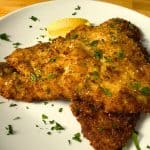Italian breaded chicken cutlets on a white plate garnished with parsley and lemon slices