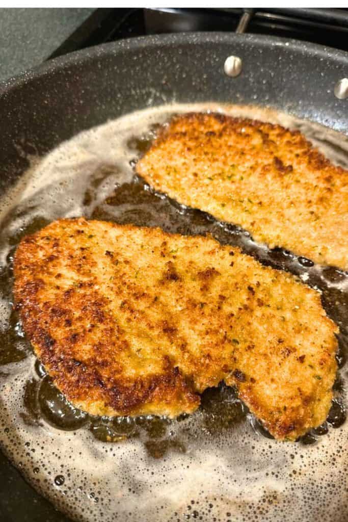 Two Italian breaded chicken cutlets frying on the stove